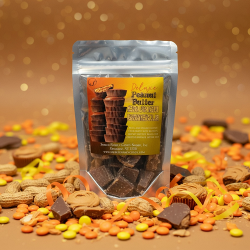 Deluxe Peanut Butter Crunch Brickle bag surrounded by peanuts, broken peanut butter cups, orange and yellow ribbons on a brown background with glitter