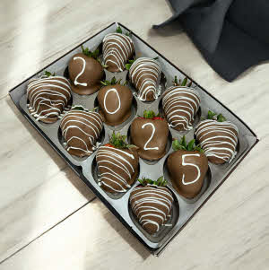 Grad Berries - milk chocolate berries with white chocolate drizzle and number chocolate on four berries in a box on a white wood countertop with graduation cap