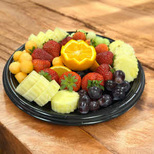 tray of fresh fruit, oranges, grapes, melon, pineapple and strawberries on a wooden counter